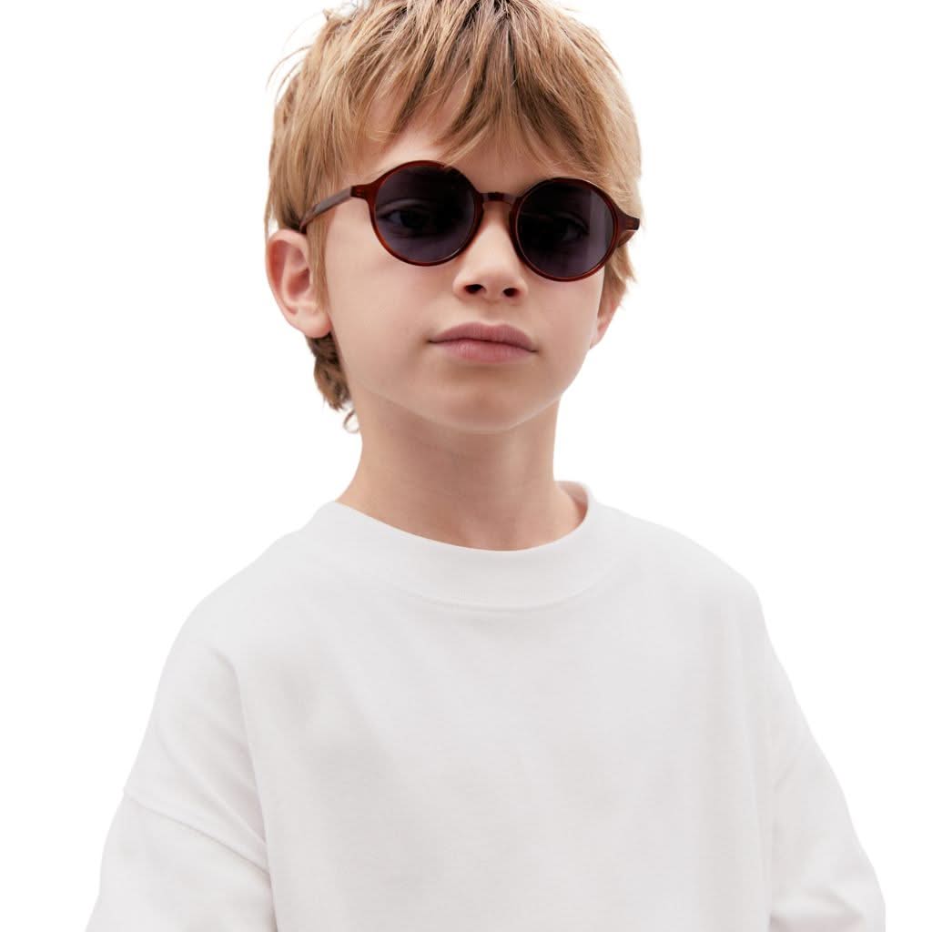 Kind trägt die Kaleos Kids Gardner col. 3 Kinder-Sonnenbrille in Havanna-Braun – erhältlich bei Brillen Schneider in München.